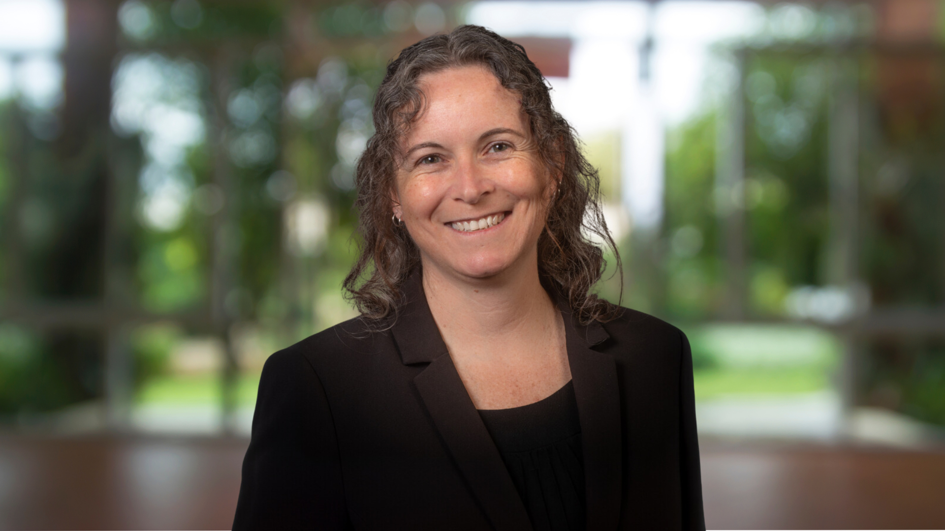 Portrait of Trish Ruebottom, a smiling White woman wearing a black blouse and jacket.