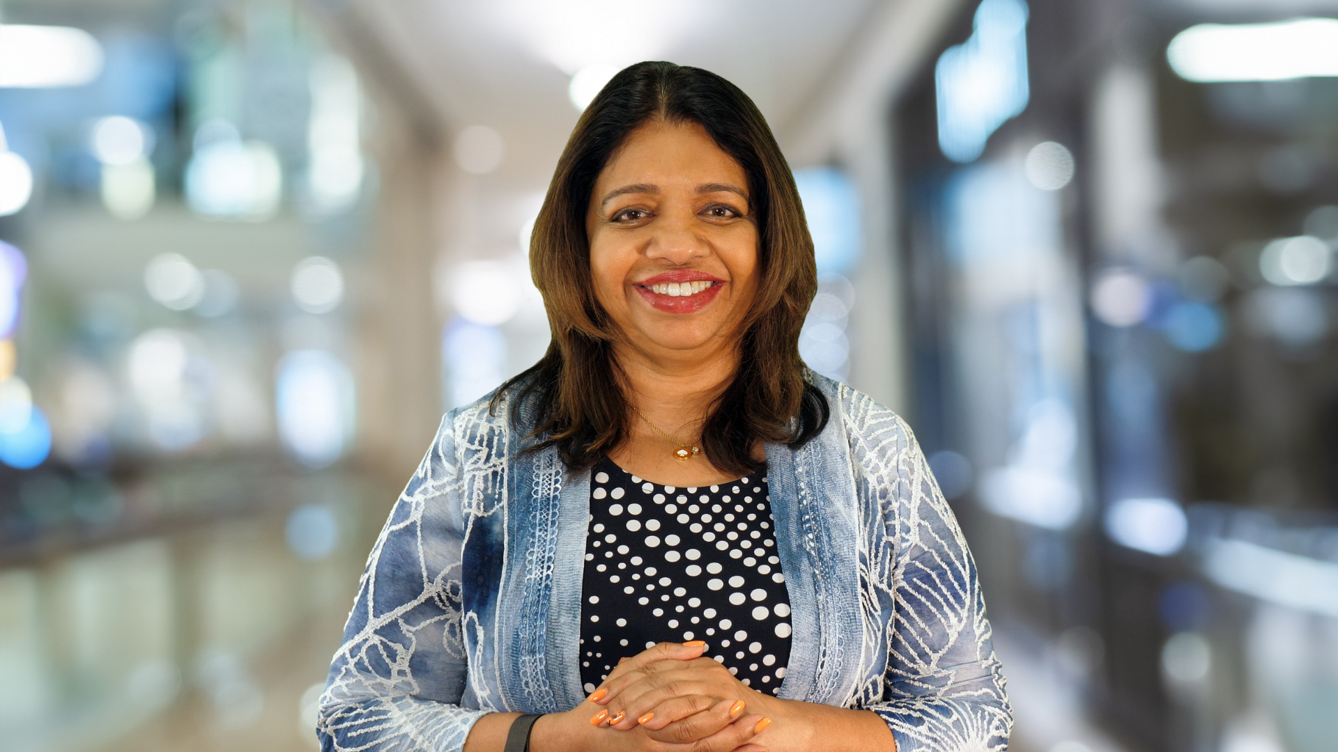 Portrait of Uma Gopinath, a smiling Indian woman in a black and white blouse with a jean-colored jacket.
