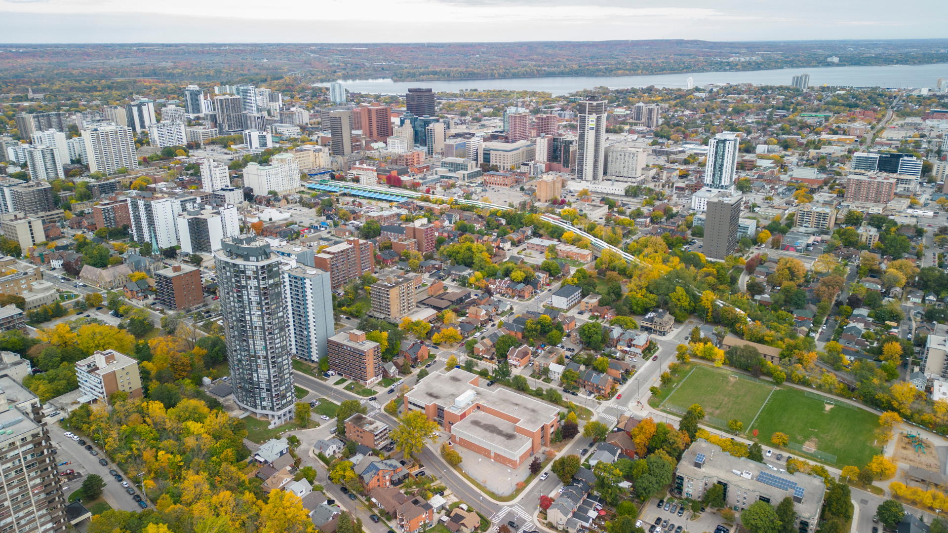 Bird's eye view of a city with many trees, parks, commercial buildings, apartments, and a river in the background.