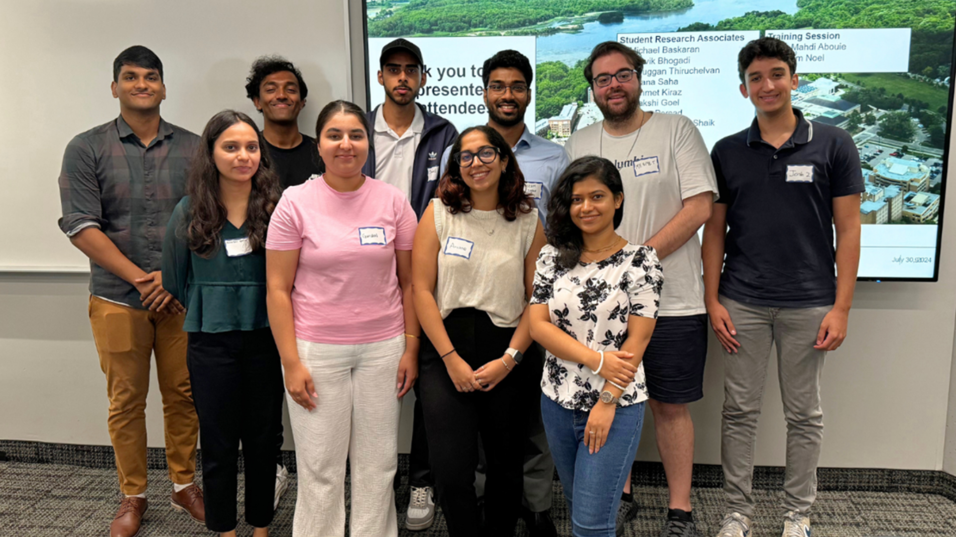 Nine young university students smile for a photo in front of a presentation slide.