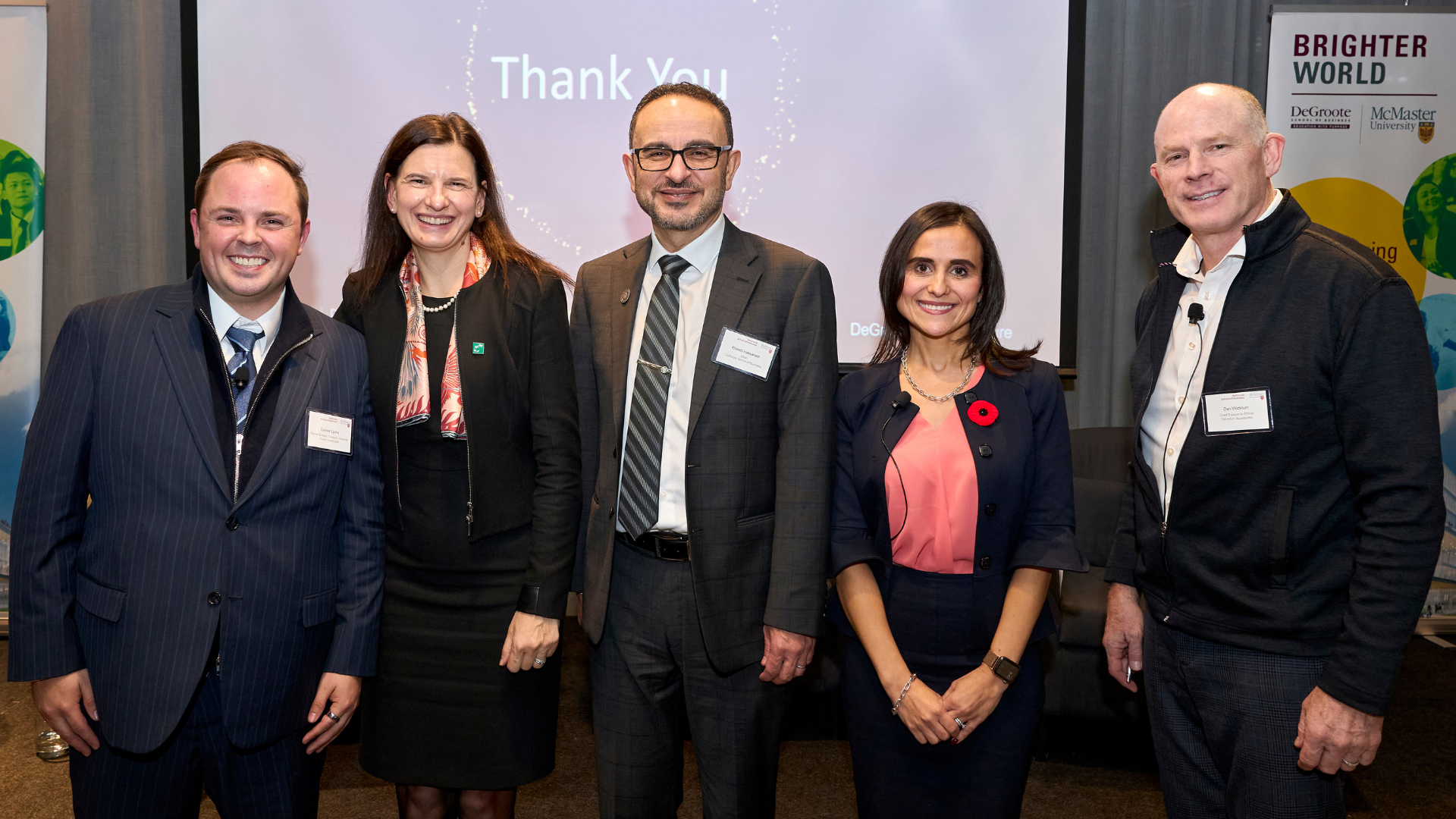 Five smiling professionals pose for a group photo in front of a "Thank You" screen and university banners.