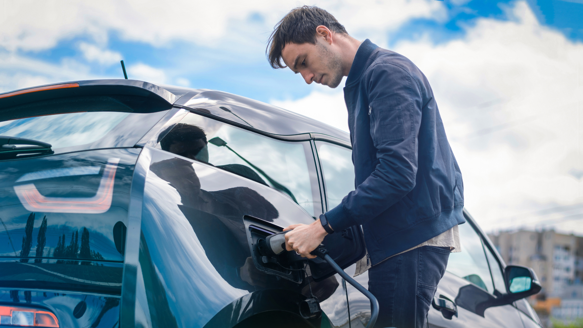 A man leaning over to plug in his electric vehicle to charge during the day.