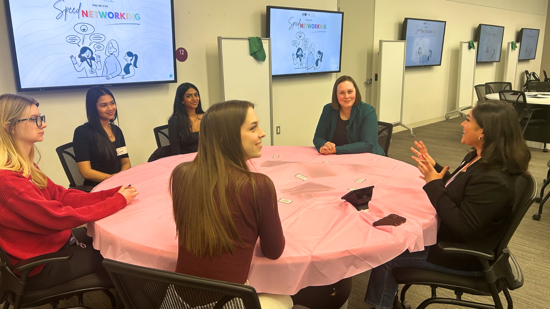 People networking at a round table with event screens.