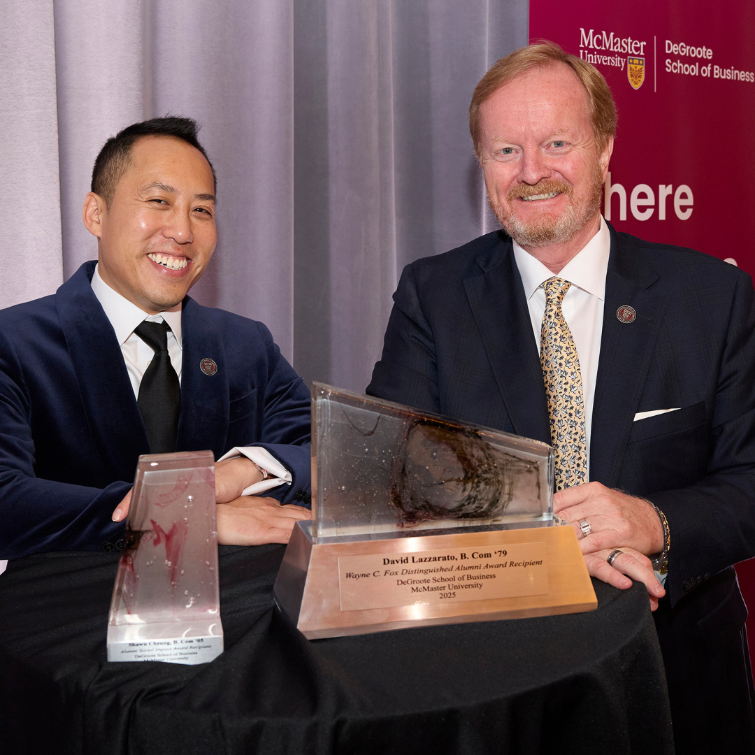 Two people in formal attire standing at a round table displaying two engraved awards.