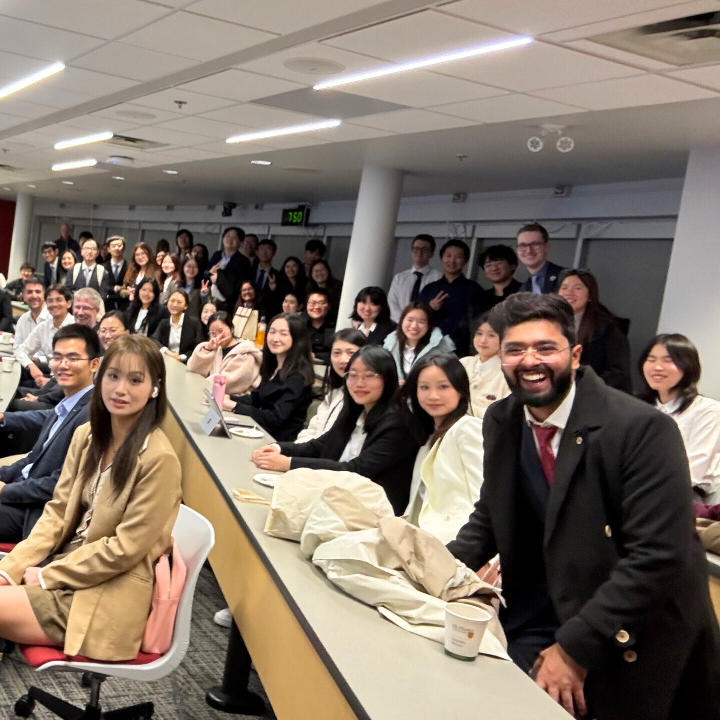 Large group of students and faculty gathered in a lecture hall, smiling toward the camera during a class or event.